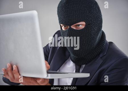 Hacking in Ihre geheimen Dateien. Konzeptionelle Aufnahme eines Mannes mit einer Maske über dem Kopf, der an einen Computer hackt. Stockfoto