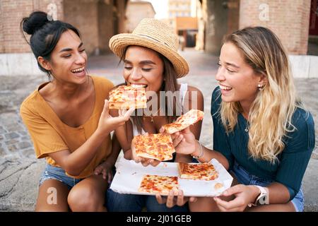 Lustige Gruppe von drei Mädchen und sie haben Spaß beim Essen Pizza in der Touristenstadt. Italienische Frau mit Straßenessen Stockfoto