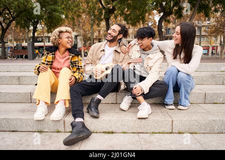 Fröhliche Freunde singen und spielen die Ukulele draußen in der Stadt. Stockfoto
