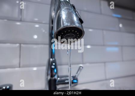 Niedriger Winkel, selektiver Makrofokus auf einem Edelstahl Küchenspüle Wasserhahn, mit Wasser in einem dünnen stetigen Strom gießen Stockfoto