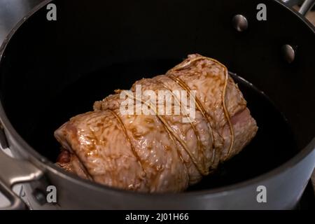 Nahaufnahme, selektive Konzentration auf einen saftigen Schweinekastall in einem großen Topf mit Sojasauce und grünen Zwiebeln Stockfoto