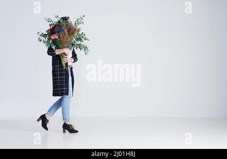 Der Alltag ist für Blumen. Studioaufnahme einer nicht erkennbaren Frau, die Blumen vor einem grauen Hintergrund hält. Stockfoto