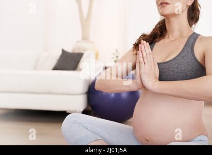 Gleichgewicht finden. Kurzer Schuss einer Schwangeren, die zu Hause meditiert. Stockfoto