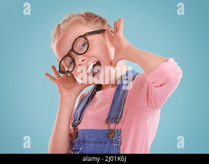 Diese Brille lässt mich niedlich fühlen. Studioaufnahme eines kleinen Mädchens mit einer Hipster-Brille auf blauem Hintergrund. Stockfoto