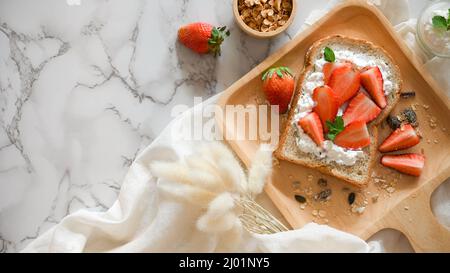 Lecker gesunder Toast mit Erdbeeren, Samen, Müsli und Quark auf Holzplatte auf weißem Marmorboden. Stockfoto