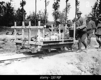 Fünf deutsche Kriegsgefangene schieben eine LKW-Plattform entlang einer Reihe von Gleisen. Zwei verwundete britische Soldaten liegen verdeckt auf dem Lastwagen. Stockfoto