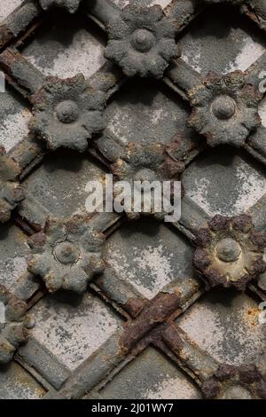 Nahaufnahme von verrosteten mittelalterlichen Gitterrosten an der grauen Stahltür. Stockfoto