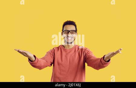 Glücklicher junger Mann in einer Brille lächelt und breitet seine Arme weit aus, um jemanden zu umarmen Stockfoto