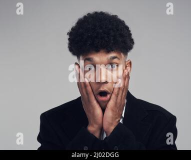 Druckmaschine alarmieren. Studioportrait eines selbstbewussten jungen Geschäftsmannes, der vor grauem Hintergrund schockiert aussieht. Stockfoto