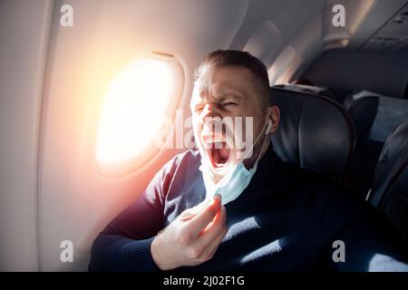 Angst vor dem Fliegen im Flugzeug und Höhe Tourist Mann in sichere medizinische Maske. Konzept Aerophobie oder Aviophobie. Stockfoto