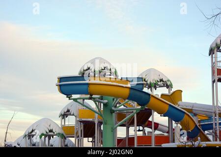 Ein schönes und helles Bild von Entspannung und Unterhaltung. Schöne wassergelbe, blaue, farbige und helle Rutschen mit Palmenabdeckung aus Kunststoff Stockfoto