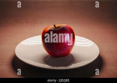 Reifer roter Apfel auf einem weißen Teller auf einem Holztisch. Stockfoto