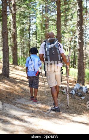 Bei einem Spaziergang durch den Wald. Glücklicher afrikanischer Vater und Sohn, die gemeinsam im Wald spazieren gehen. Stockfoto