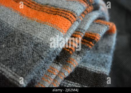 Dinge, Gegenstände, Kleidung aus Naturstoffen. Ein schöner Herrenpullover ist in Form von orangefarbenen, grauen, dunkelgrauen, schwarzen Streifen hergestellt, die. Stockfoto