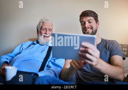 Wir heißen Opa im Zeitalter der Technologie willkommen. Aufnahme eines jungen Mannes, der seinem älteren Großvater zeigt, wie man ein Tablet benutzt, während er zu Hause auf der Couch sitzt Stockfoto