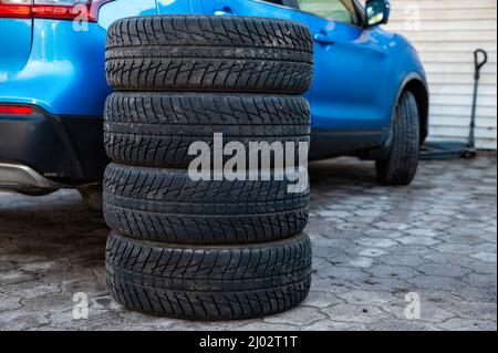 Satz von Winterreifen neben dem Auto im Radservice, das Konzept des saisonalen Reifenwechsels Stockfoto