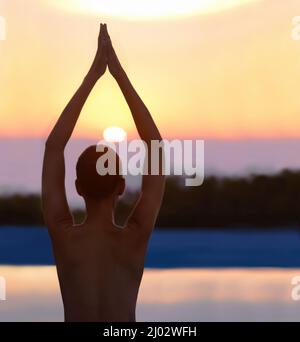 Ruhe in der Natur finden. Eine schöne junge Frau in einer Yoga-Pose bei Sonnenuntergang. Stockfoto