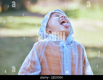Wie Wasser aus dem Himmel. Aufnahme eines kleinen Mädchens, das ihre Zunge herausstreckt, um die Regentropfen in ihrem Mund zu fangen.