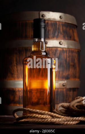 Flasche mit Whiskey, Cognac oder goldenem Rum. Vor einem alten Holzfass Stockfoto