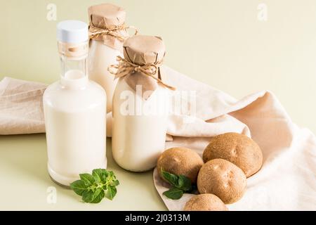 Drei Glasflaschen mit veganer Pflanzenmilch aus Kartoffelknollen auf beigefarbenem pastellfarbenem Hintergrund. Das Konzept der gesunden Ernährung. Getränkersatz Stockfoto