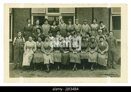 Original-Postkarte aus der Zeit des 1. Weltkriegs mit einer großen Gruppe von Fabrikarbeitern, möglicherweise Munitionsarbeitern, da die Frau 2. Links in der hinteren Reihe das Munitionsabzeichen „im Kriegsdienst“ trägt. Foto von F. Taylor, Wembley, London, Großbritannien um 1918. Stockfoto