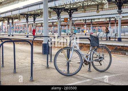 Ein Fahrrad mit einem Korb, der auf einer Bahnhofsplattform geparkt ist. Andere Plattformen mit historischen Vordächern sind im Hintergrund. Stockfoto