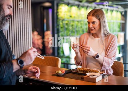 Sushi-Meister lehrt junge Frauen, wie man Essstäbchen im Sushi-Restaurant verwendet. Stockfoto