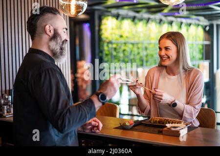 Sushi-Meister lehrt junge Frauen, wie man Essstäbchen im Sushi-Restaurant verwendet. Stockfoto