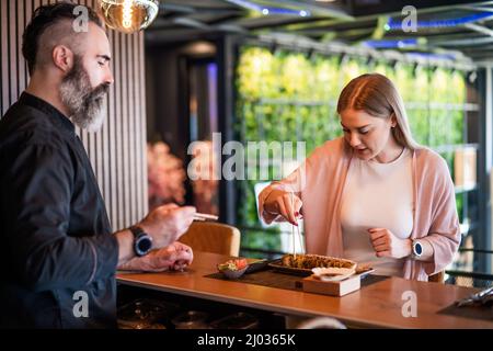 Sushi-Meister lehrt junge Frauen, wie man Essstäbchen im Sushi-Restaurant verwendet. Stockfoto