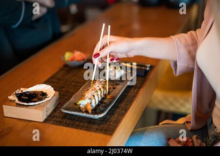 Nahaufnahme einer Frau, die im Sushi-Restaurant Umami-Sushi mit Essstäbchen isst. Stockfoto