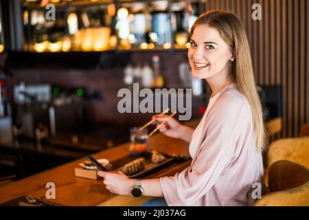 Glückliche Frau isst Sushi mit Essstäbchen im Sushi-Restaurant. Stockfoto