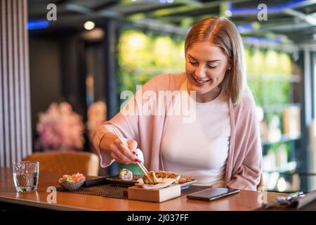 Glückliche Frau isst Sushi mit Essstäbchen im Sushi-Restaurant. Stockfoto