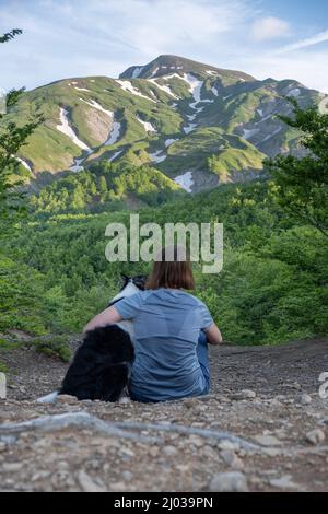 Ein Mädchen sitzt neben und umarmt ihren Border Collie Hund starrt auf eine Berglandschaft des Cusna Mountain, Emilia Romagna, Italien, Europa Stockfoto