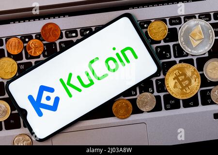 Ein Smartphone mit dem KuCoin Logo Metallmünzen, Bitcoin, ethereum auf einer Laptop-Tastatur. Stockfoto