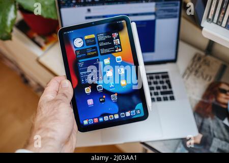 Paris, Frankreich - 25. Oktober 2021: POV männliche Hand hält neue neueste iPad Mini pro Professional zeigt alle Apps auf dem Display mit MacBook pro Laptop im Hintergrund Stockfoto