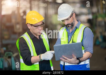 Chief Engineer im Gespräch mit Mitarbeitern, die in der Fabrik detailliert auf Laptops blicken. Stockfoto