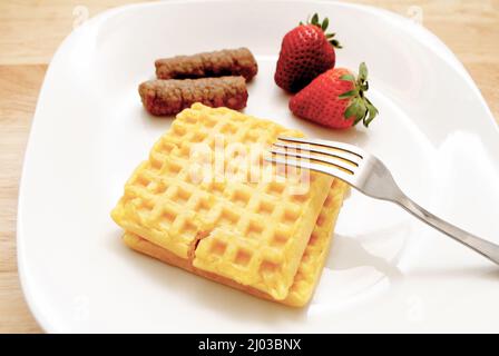 Waffeln und zwei Schweinewurst-Links auf einem weißen Teller mit frischen Erdbeeren Stockfoto