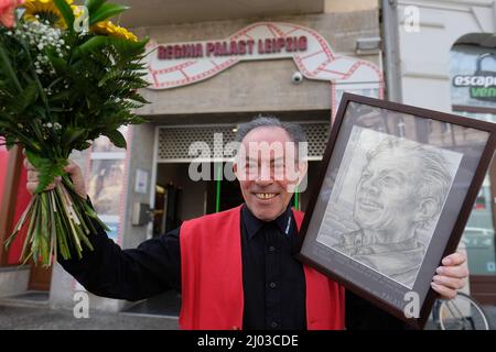 Leipzig, Deutschland. 16. März 2022. Hans Höher, Eisverkäufer im Kino, steht mit Blumen und einem Porträt vor dem Regina-Palast. Der 82-Jährige war früher als Filmvorführer tätig und wurde nach dem Fall der Berliner Mauer in verschiedenen Kinos als Eisverkäufer bekannt. Jetzt geht er in den Ruhestand. Quelle: Sebastian Willnow/dpa-Zentralbild/dpa/Alamy Live News Stockfoto