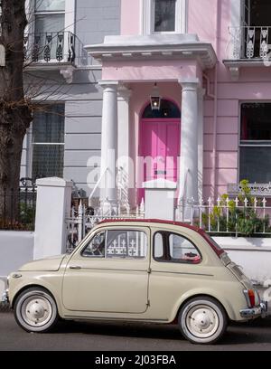 Beigefarbener Oldtimer Fiat 500, der vor einem Haus mit einer rosafarbenen Tür in einer Wohnstraße in Notting Hill, West-London, Großbritannien, geparkt ist. Stockfoto