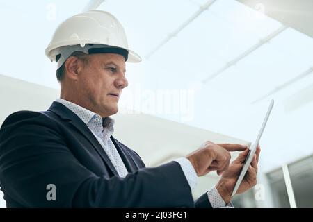 Einige kleine Änderungen vornehmen. Aufnahme eines fokussierten, professionellen Architekten, der neben einer Entwicklungsstelle steht, während er ein digitales Tablet in einem verwendet Stockfoto