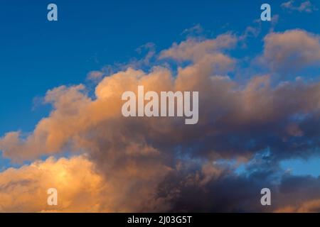 Farbenfrohe, weiche, wispy-orange Wolken vor einem blauen Winterhimmel Stockfoto