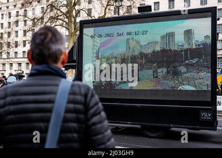 Ein Passant sieht Szenen der Zerstörung auf einer Leinwand bei Protesten in der Downing Street zur Unterstützung der Ukraine nach der russischen Invasion am 2022. März Stockfoto
