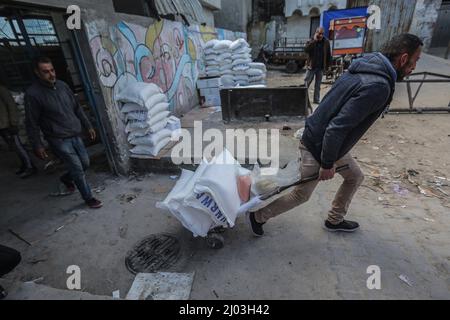 Gaza-Stadt, Palästinensische Gebiete. 16. März 2022. Die Palästinenser sammeln Nahrungsmittelhilfe von einem Verteilungszentrum, das vom Hilfswerk der Vereinten Nationen (UNRWA) betrieben wird. Die Lebensmittelpreise in Gaza-Stadt sind nach dem russischen Einmarsch in die Ukraine angestiegen. Einige Flüchtlinge verkaufen die Nahrungsmittelhilfe, die Mehl, Speiseöl, Reis, Linsen und Milch umfasst, Geld für ihren Lebensunterhalt zu sichern. Kredit: Mohammed Talatene/dpa/Alamy Live Nachrichten Stockfoto