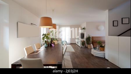 Großes Wohnzimmer mit Esstisch, hellen Stühlen und einem großen Sofa. Große, helle Fenster. Modernes Design-Apartment Stockfoto