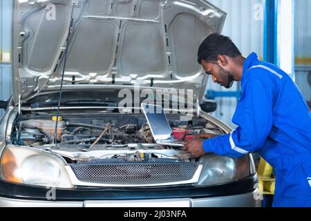 Automechaniker mit Laptop bei der Überprüfung von Automotor oder -Schaltung in der Garage - Konzept von Profi-, Technologie-, Know-how- und Wartungsservice. Stockfoto