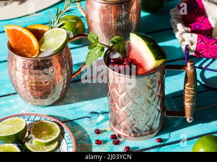 Erfrischende Cocktails, garniert mit frischem Obst und Kräutern, bei hellem Sonnenlicht. Stockfoto