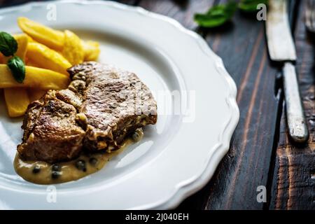 Gegrillter Schweinehals mit Pfeffersauce und Pommes auf einem Holztisch Stockfoto