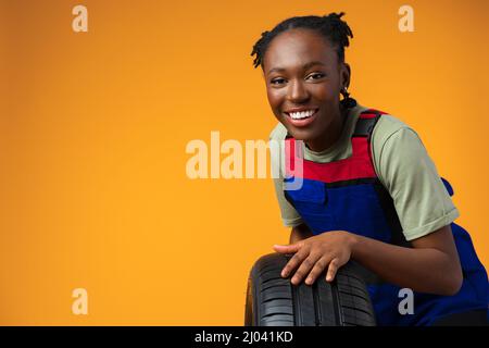 Porträt einer lächelnden schwarzen Mechanikerin, die im Studio mit neuen Autoreifen posiert Stockfoto