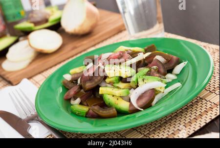 Salat aus schwarzen Tomaten, Avocado und Zwiebeln auf grünem Teller Stockfoto