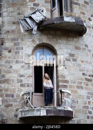 Eine Frau steht in der Tür des zerstörten Balkons einer alten verlassenen Burg. Reise durch die historischen Sehenswürdigkeiten des Kaukasus Stockfoto